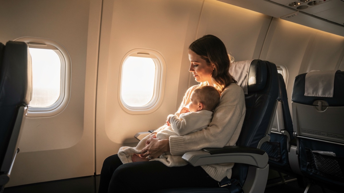 Mãe segurando bebê no colo na poltrona do avião ao lado da janela